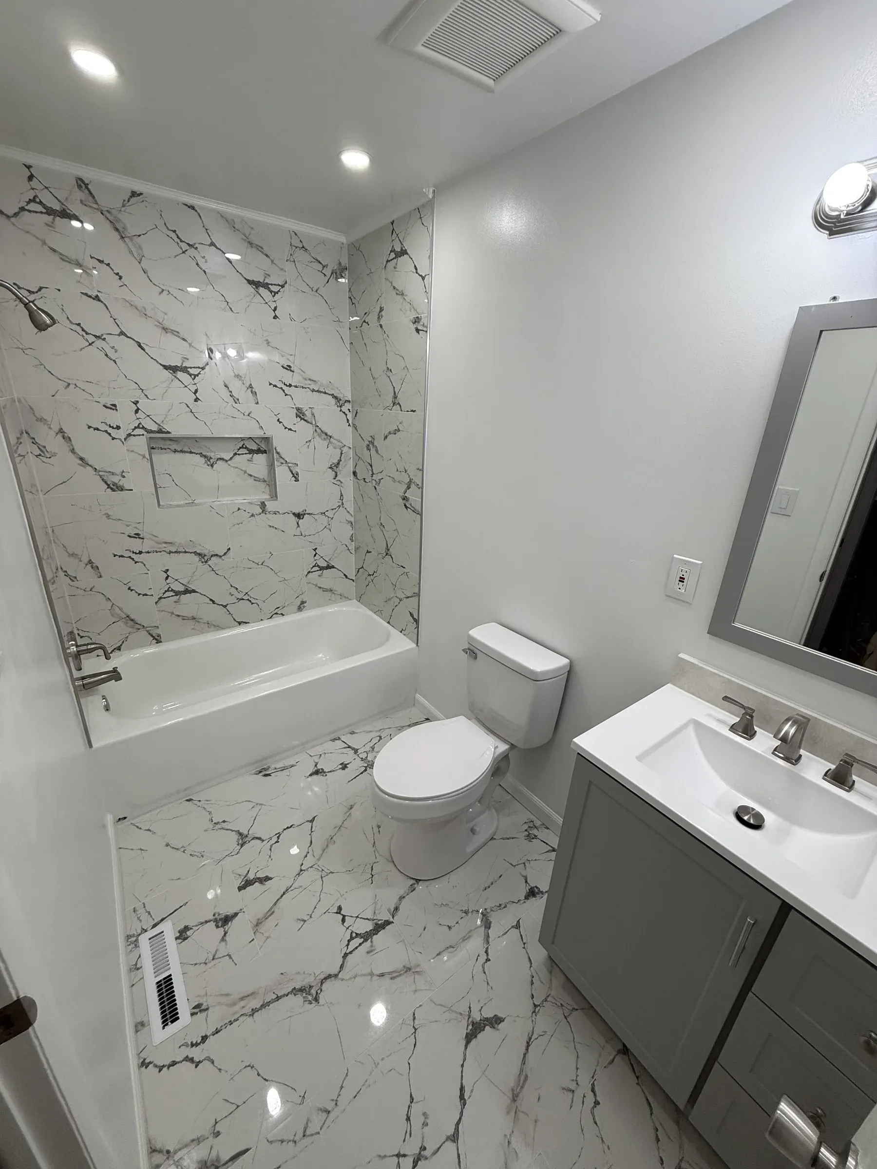 Master bathroom renovation with marble-surround tub-shower combo, niche, white quartz countertop and modern gray vanity, Delaware