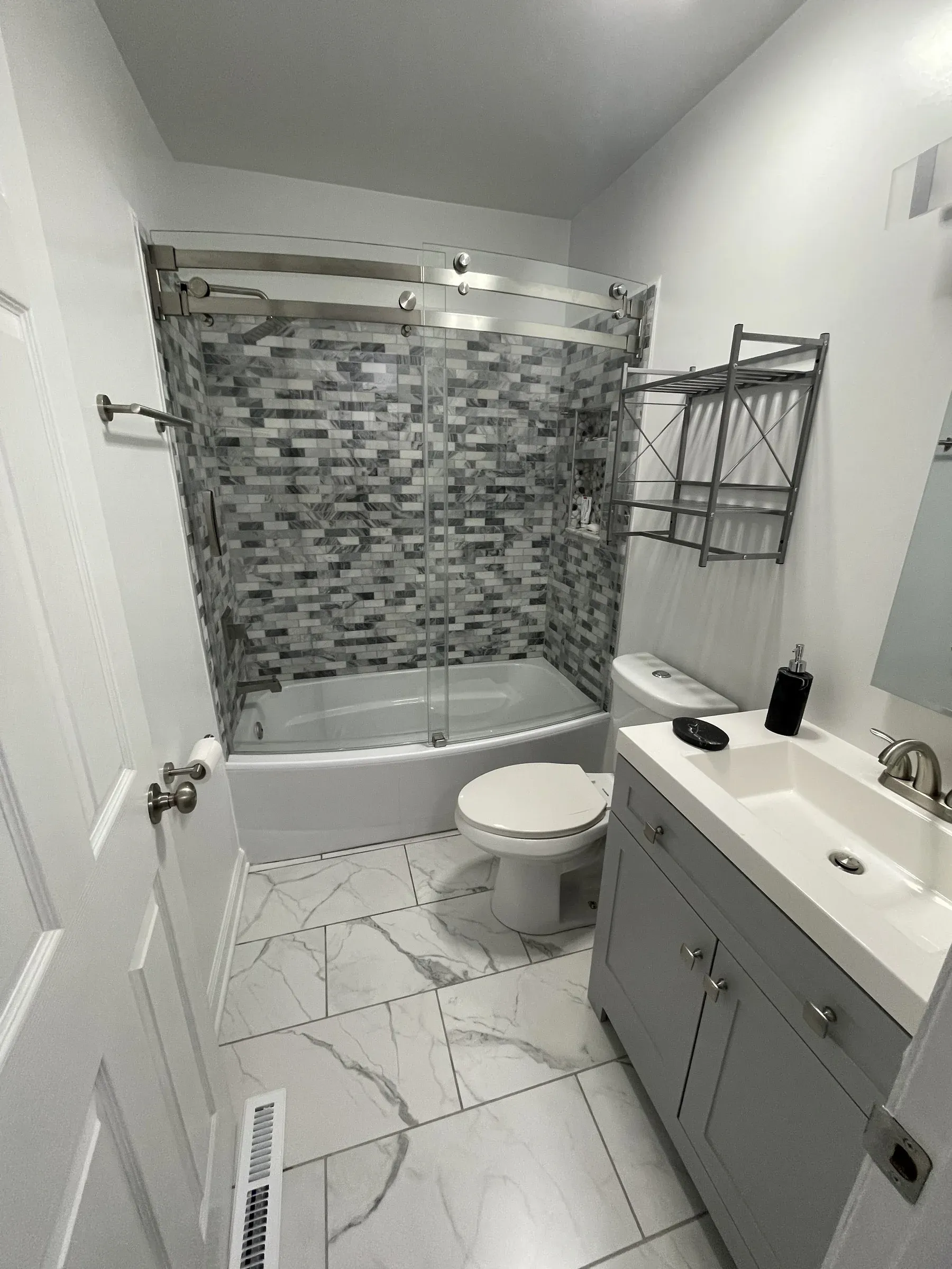 Tub and shower remodel with stacked-stone mosaic accent, frameless glass enclosure and shaker gray vanity built by Zavala & Sons