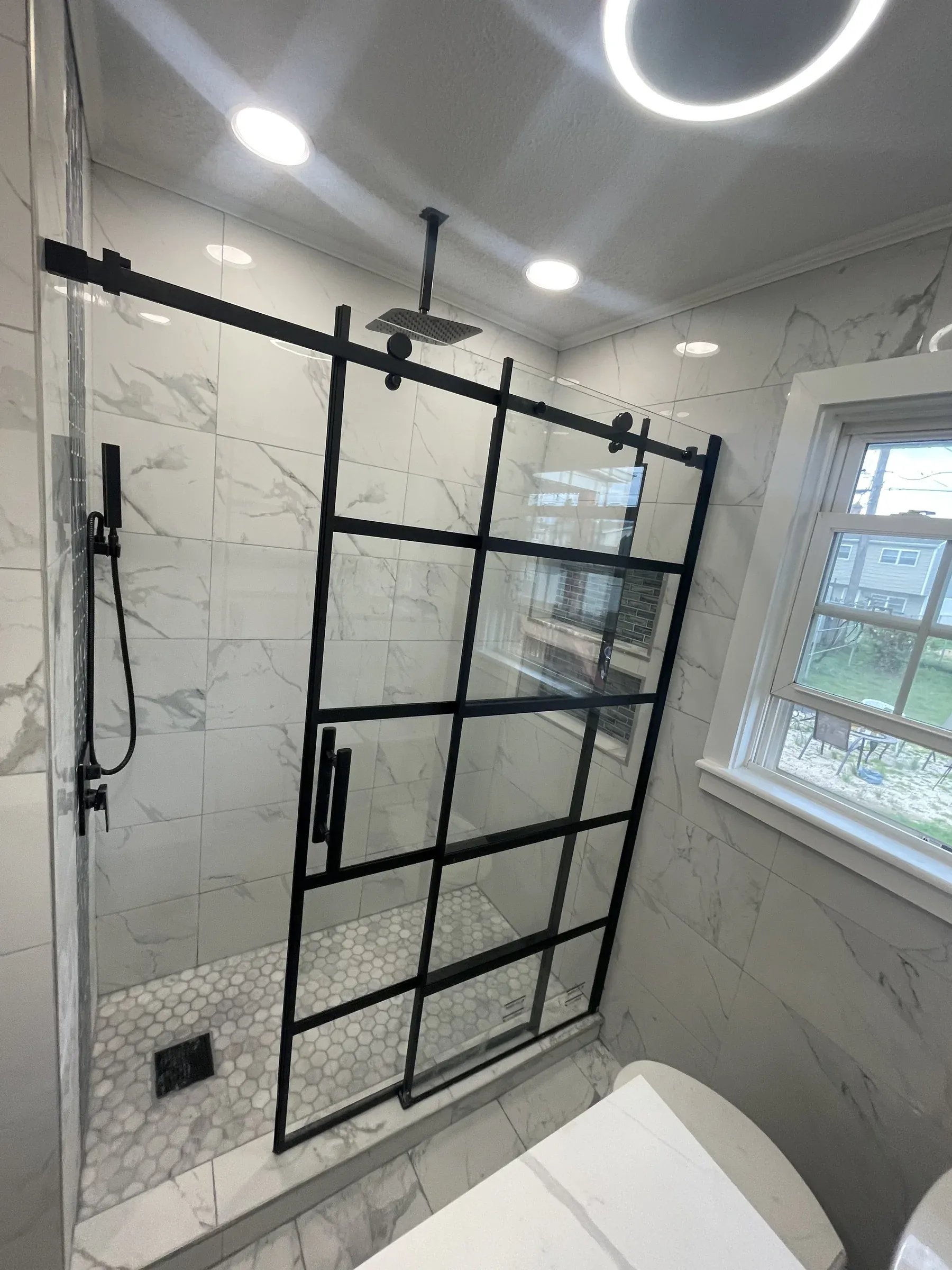 Industrial walk-in shower with black-framed glass door, white marble tile and penny-round mosaic floor — bathroom remodel near Wilmington DE